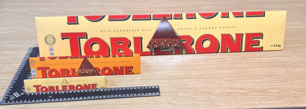 3 sizes of Toblerone on a wooden desk with a black square ruler